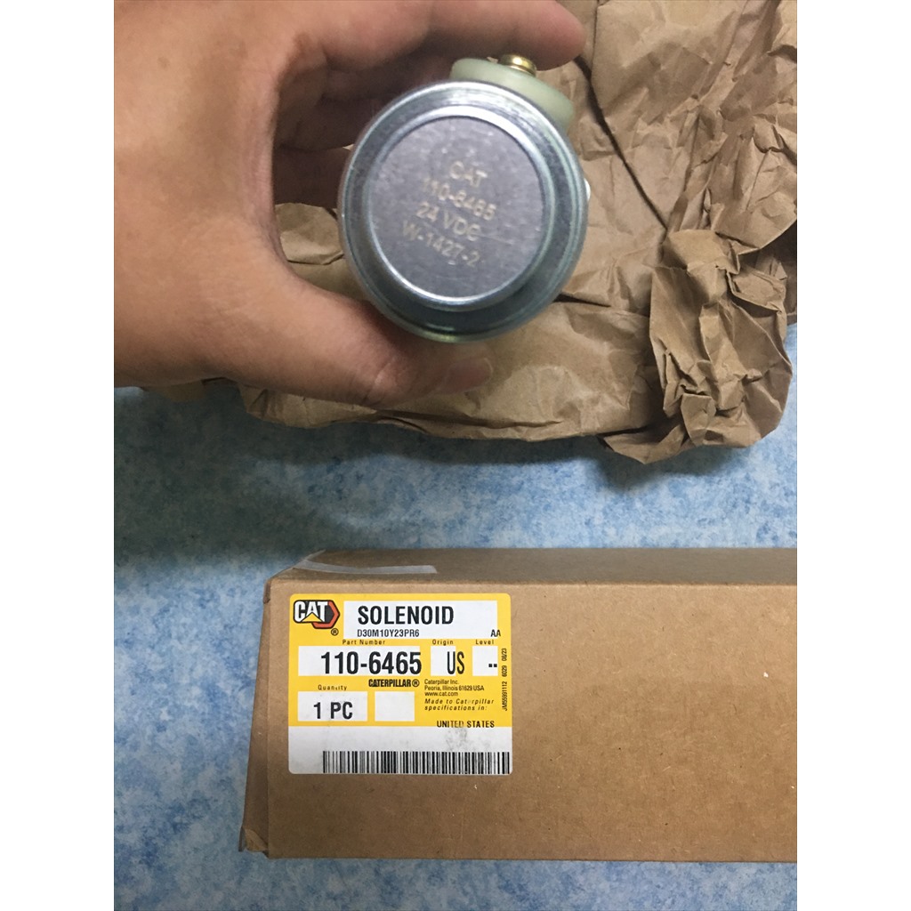 110-6465 Solenoid - round solenoid end held above a parts label
